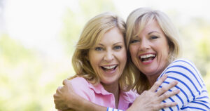 Two mature women smiling and hugging showing off their cosmetic dentistry work.
